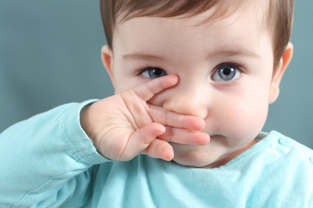 bebê de blusa azul coçando o nariz com uma das mãos