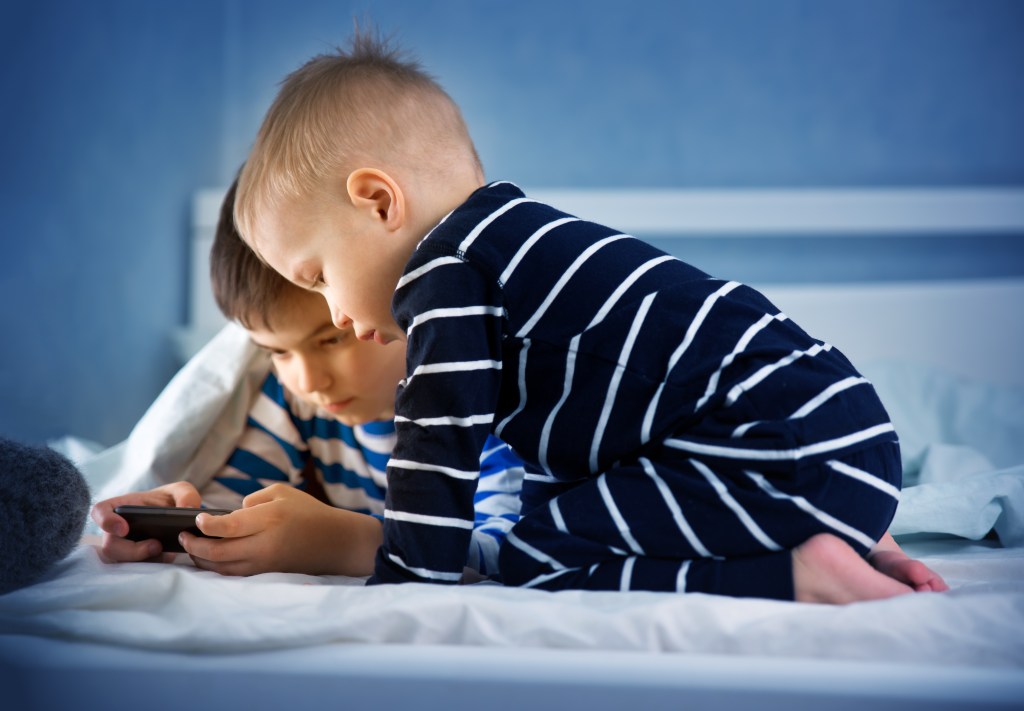 Duas crianças, meninos, na cama olhando um celular