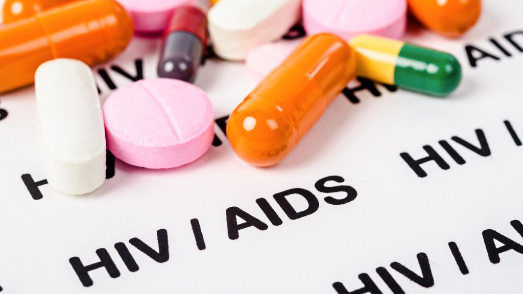 comprimidos de várias cores colocados sobre um papel em que se lê HIV/AIDS