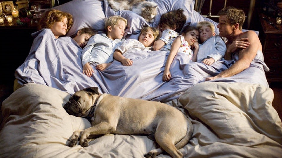 Cena do filme: pais e muitos filhos deitados na mesma cama, também com um cachorro