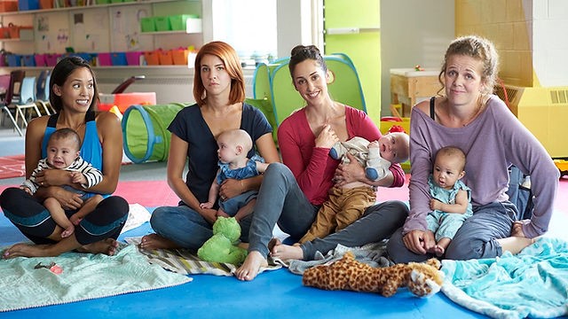Cena da série: quatro mães estão sentadas com seus bebês no colo.